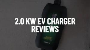 White text "2.0 KW EV CHARGER REVIEWS" overlaid on a blurry image of a dark grey Battery Tender eCharge EV Charger with a digital display, on a light grey textured surface.