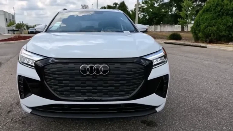 Front view of a white 2025 Audi Q4 e-tron with black grille, illuminated headlights, and modern electric design
