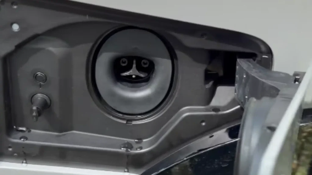 Close-up view of the built-in NACS charging port on a white 2026 Lexus RZ electric vehicle, showing a circular black charging inlet with its internal pin layout.