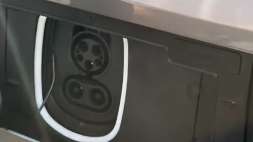 A close-up view of an open CCS Combo 1 charging port on a grey Lucid Air electric vehicle, featuring a glowing white LED light ring around the inlet.