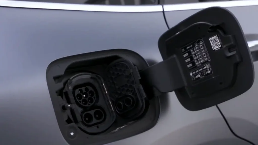 Open charging flap on a silver Mercedes-Benz EV showing a CCS Combo 2 (CCS2) charging inlet with exposed DC fast-charging pins and a rescue information QR code inside the charge door.