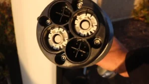 A detailed close-up of the circular face of a CHAdeMO EV charging plug, showing the two large white power ports and several smaller communication pins inside the black housing.