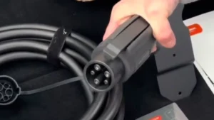 James holding a black SAE J1772 Type 1 EV charging connector, showing the five pin layout and the release latch on top.