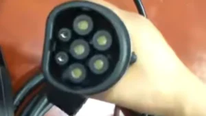 James holding a black Type 2 Mennekes EV charging connector, showing the seven pin layout and the rounded design with a flat top edge.